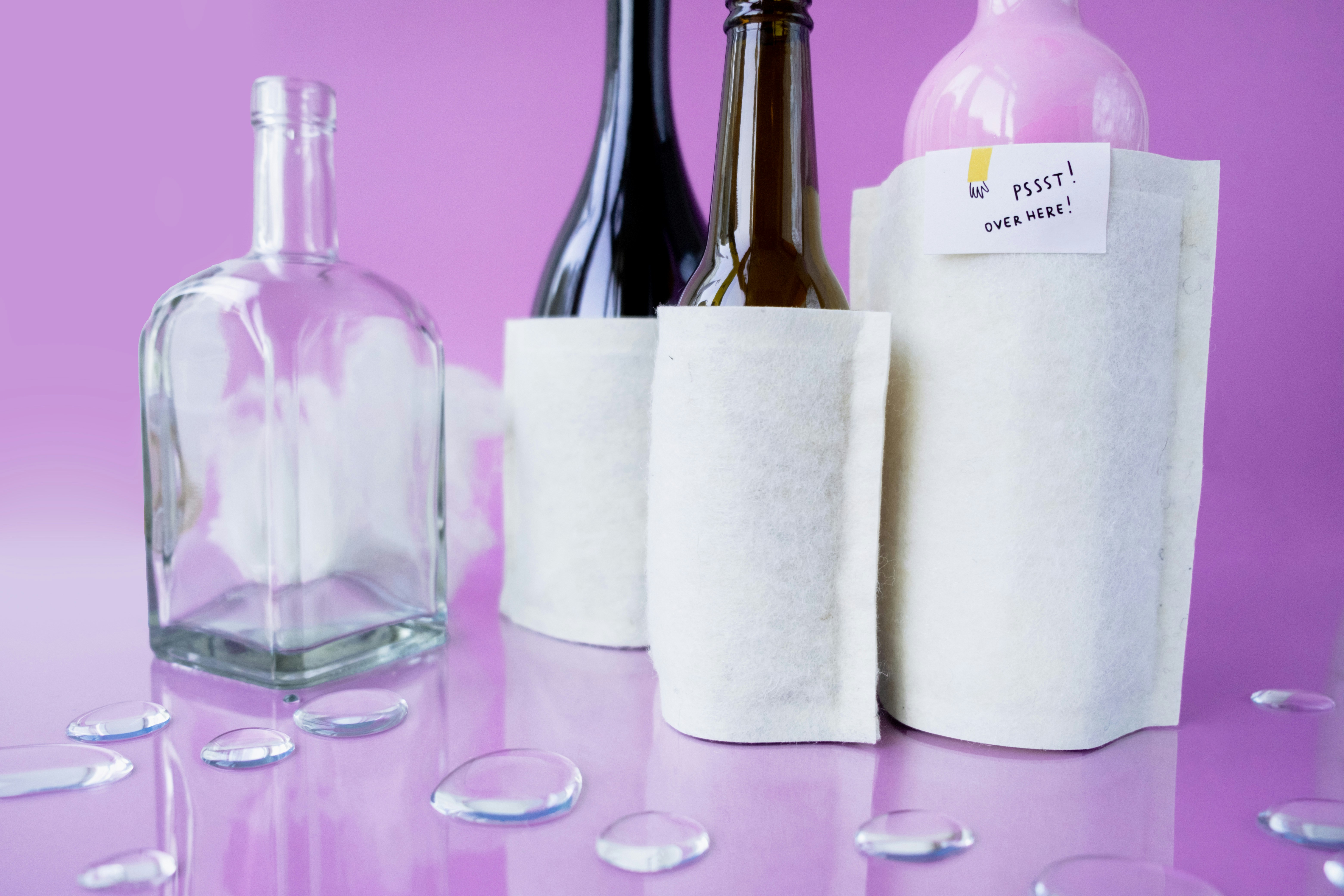Glass bottles with white sleeves on purple background.