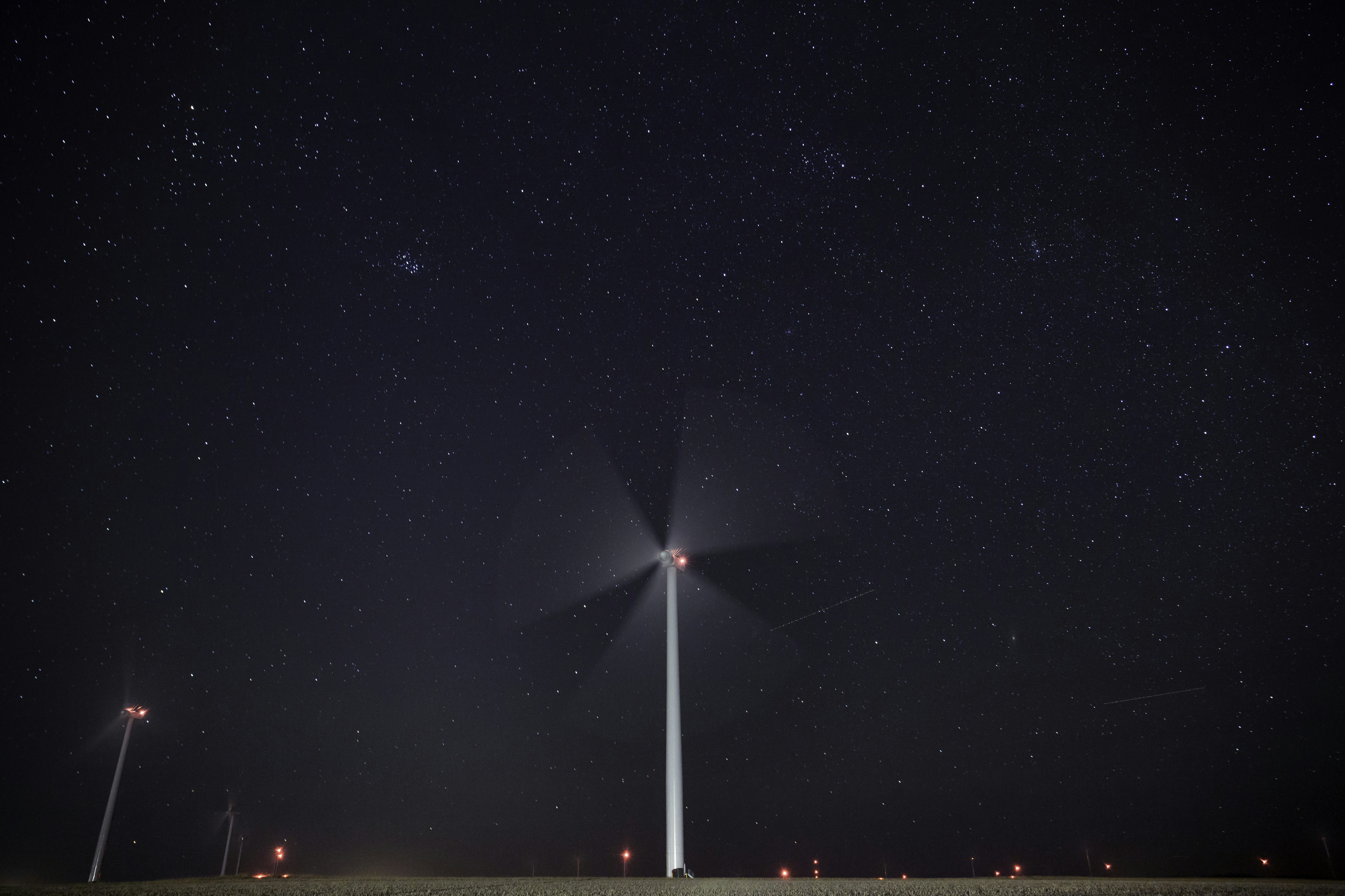 Western Kansas is known for two things: being flat and being windy. Both of those qualities make us a prime location for wind farms. People love them and people hate them. My wife hates them at night because a giant field of glowing red dots reminds her of ‘War of the Worlds’. I personally love them for multiple reasons, but for photography, they are nice in this area because they establish a looming vertical subject when we are accustomed to only never ending horizons. by Gone Greenish white tower under starry night