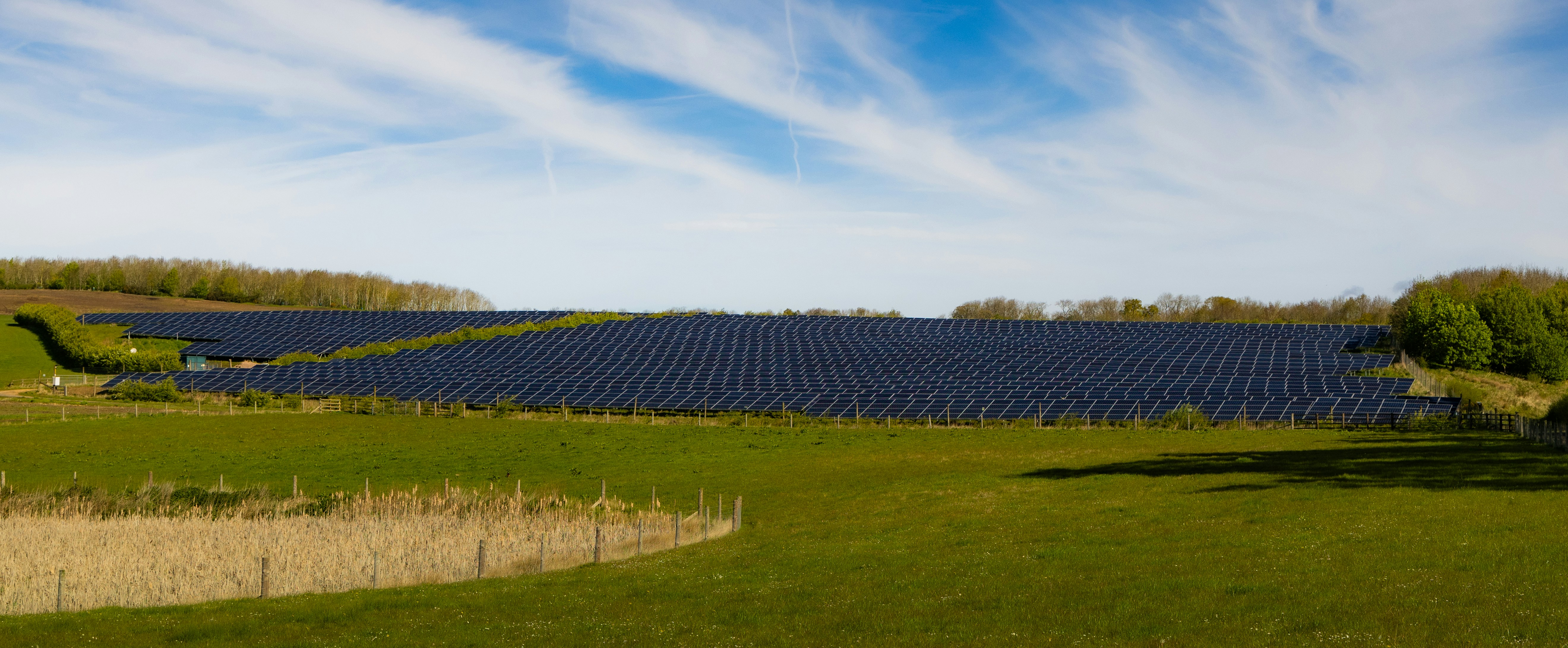 Vast solar panel field under a cloudy blue sky