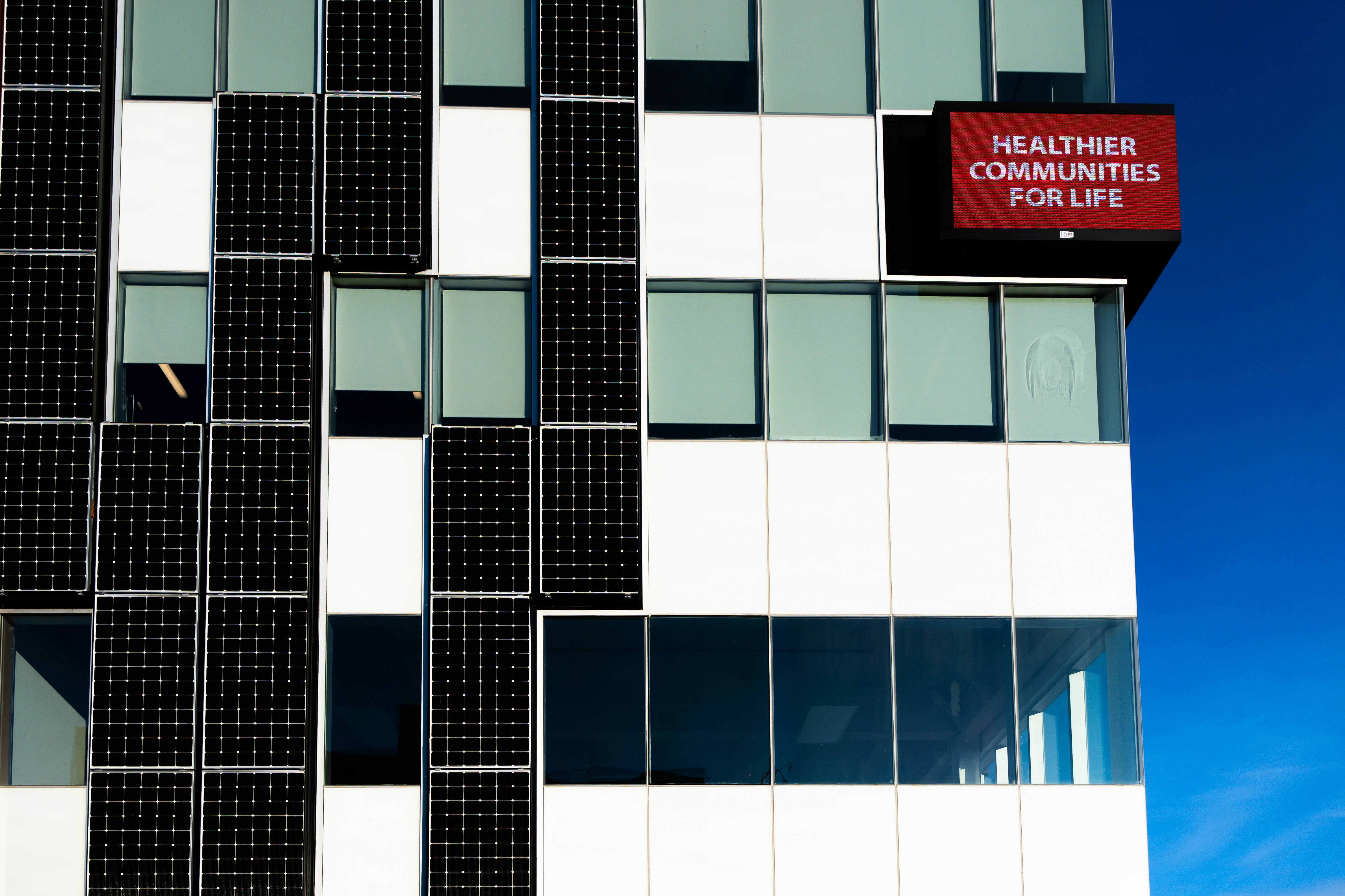 Modern building facade with solar panels and red sign.