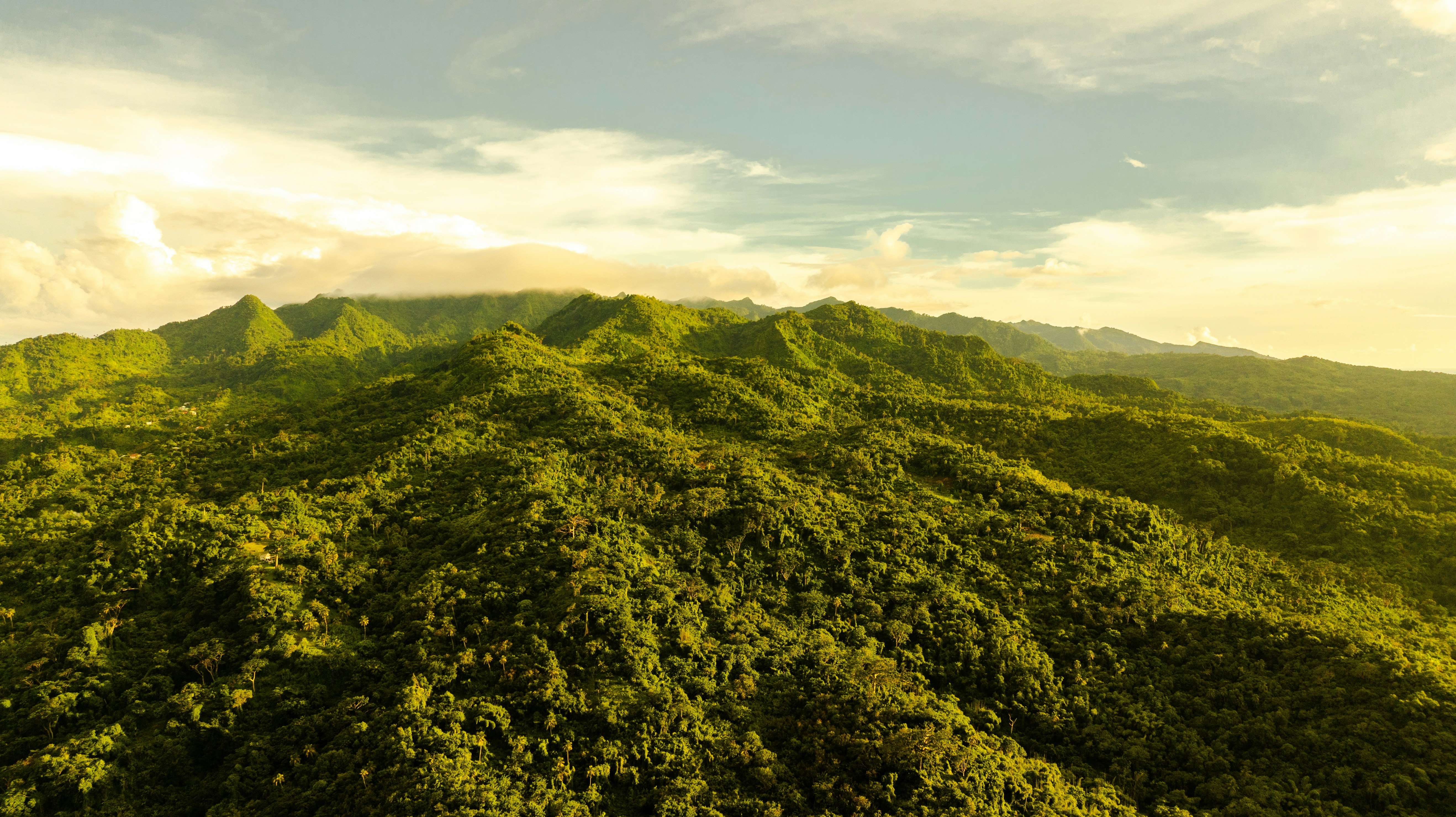 Lush green mountains under a cloudy sky at sunset.