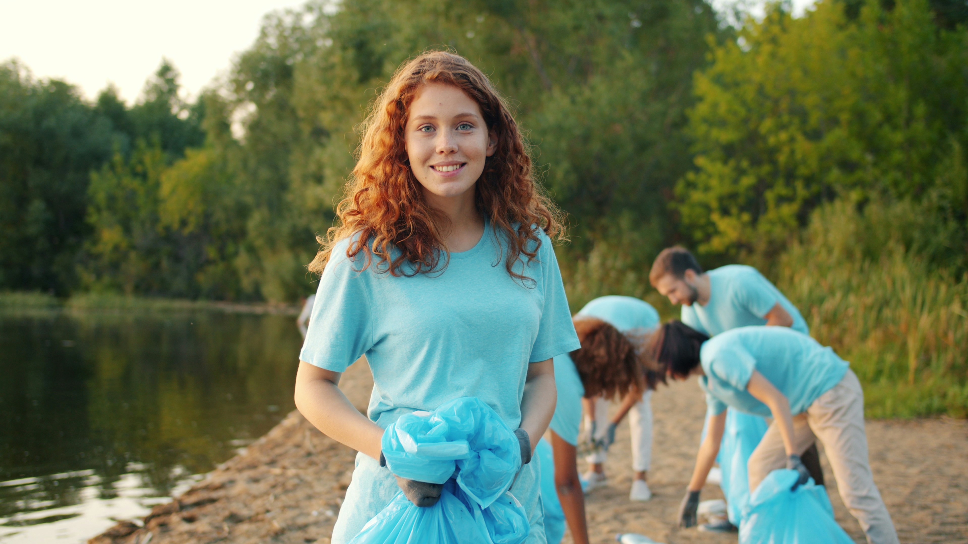 Woman smiling holding trash bags by lake