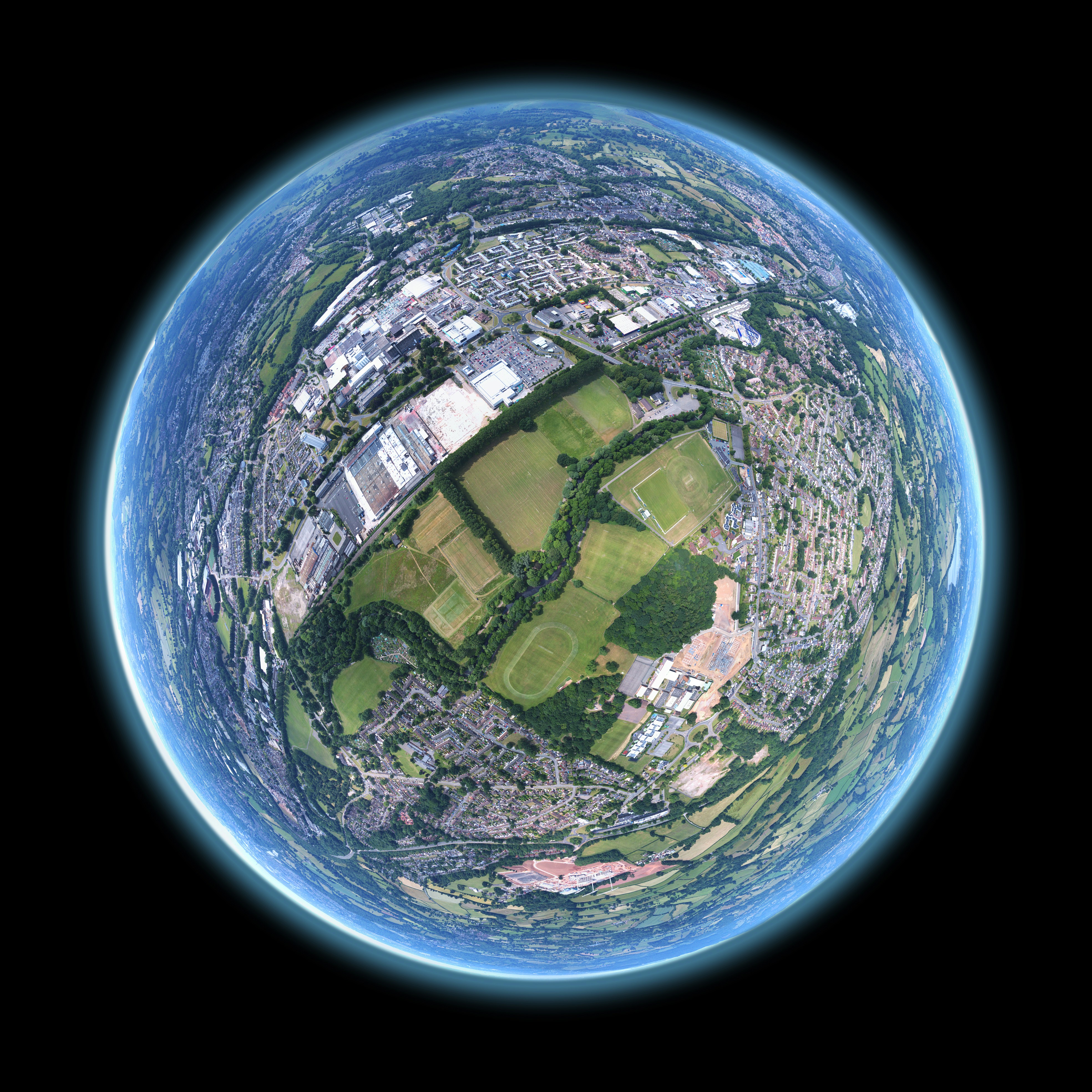 A 360 panorama stitched and warped to create the tiny planet effect. Image sequence taken by drone above a community field in Wales. by Gone Greenish fish-eye aerial shot of buildings and trees