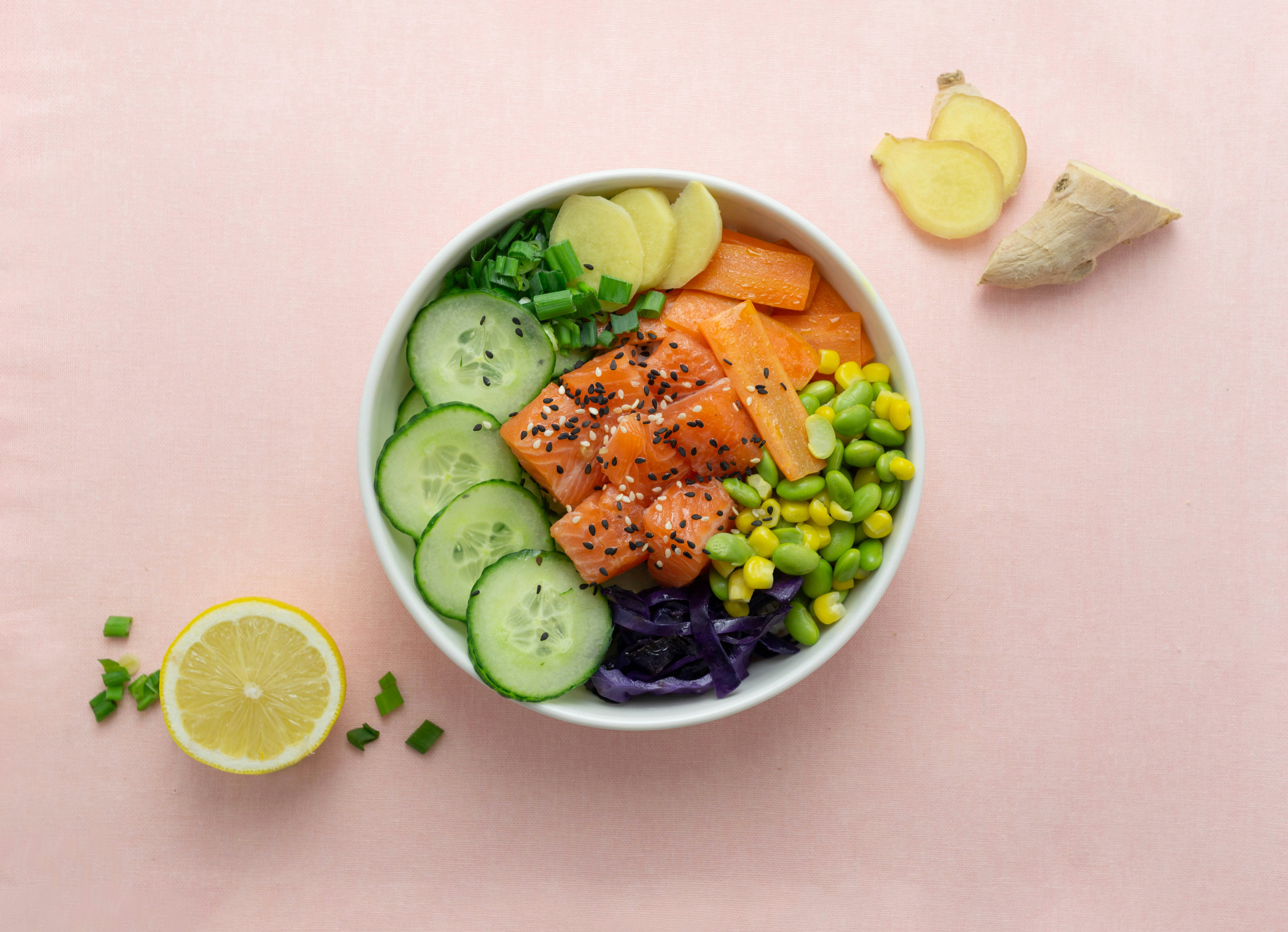 Poke bowl on a pink background by Gone Greenish sliced cucumber and sliced lemon on white ceramic bowl