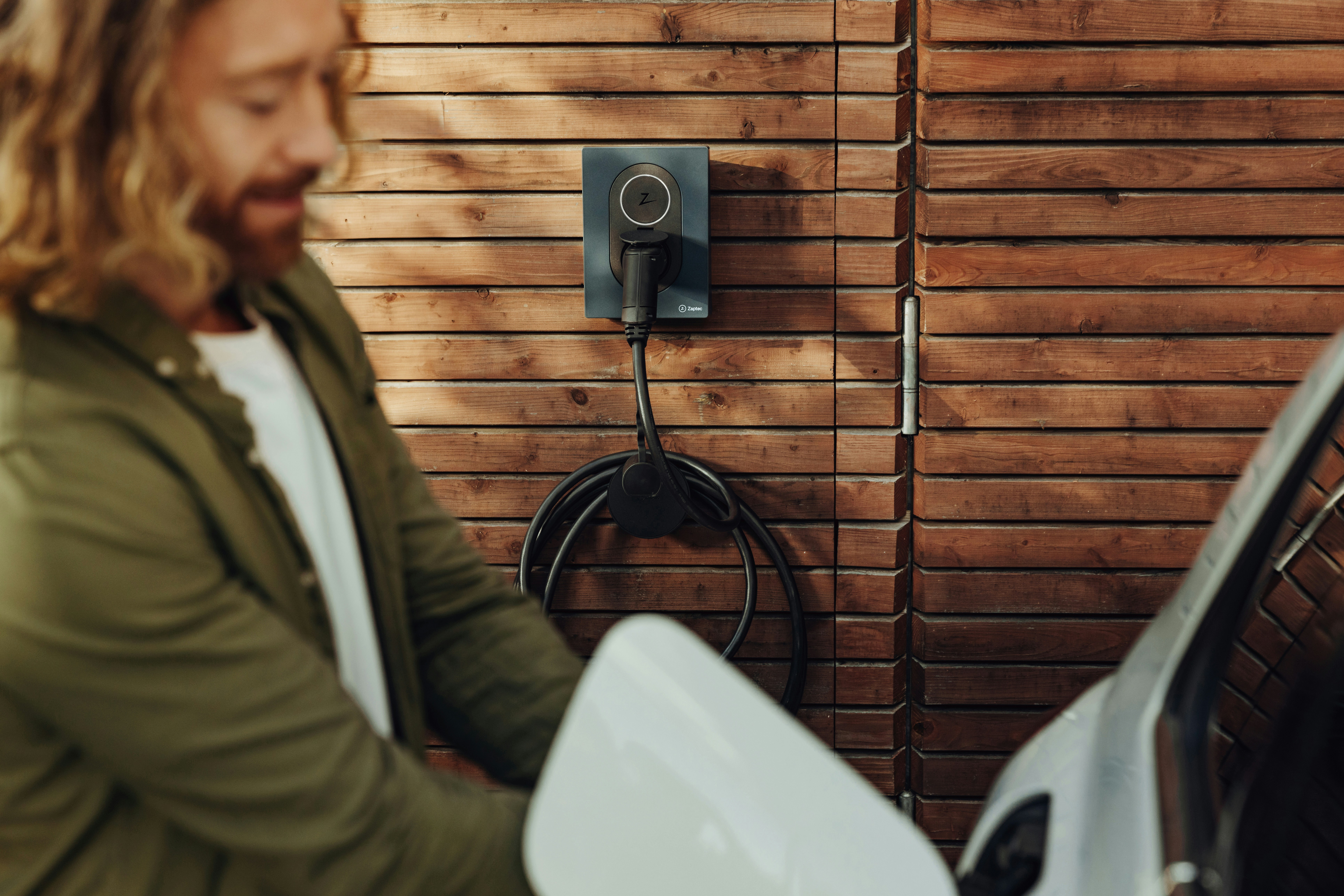 The beautifully designed and amazing Zaptec Go, home charger for electric cars. photographer: Joel Heyd by Gone Greenish a man standing next to a white toilet in front of a wooden wall