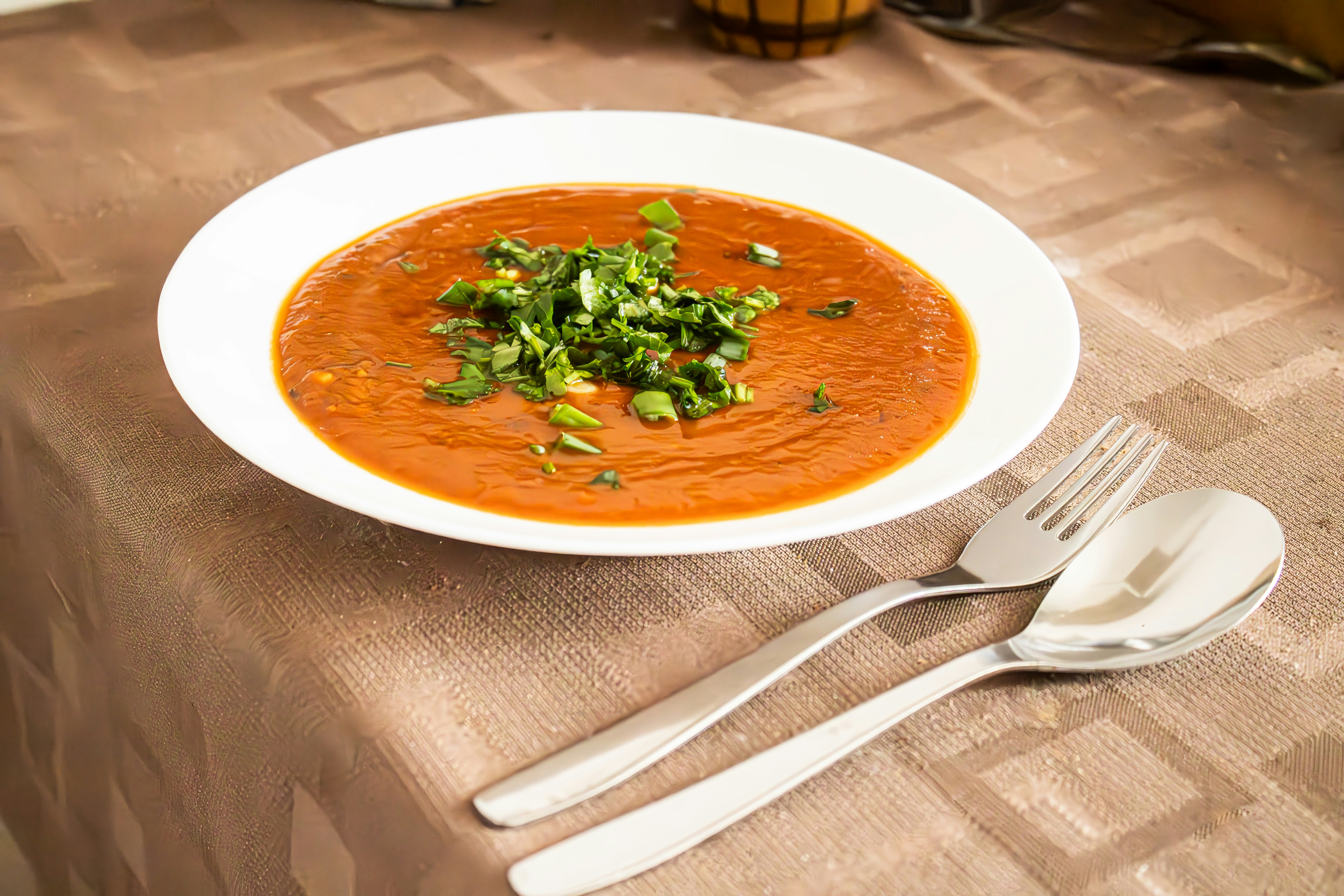 Bowl of tomato soup with fresh herbs and cutlery