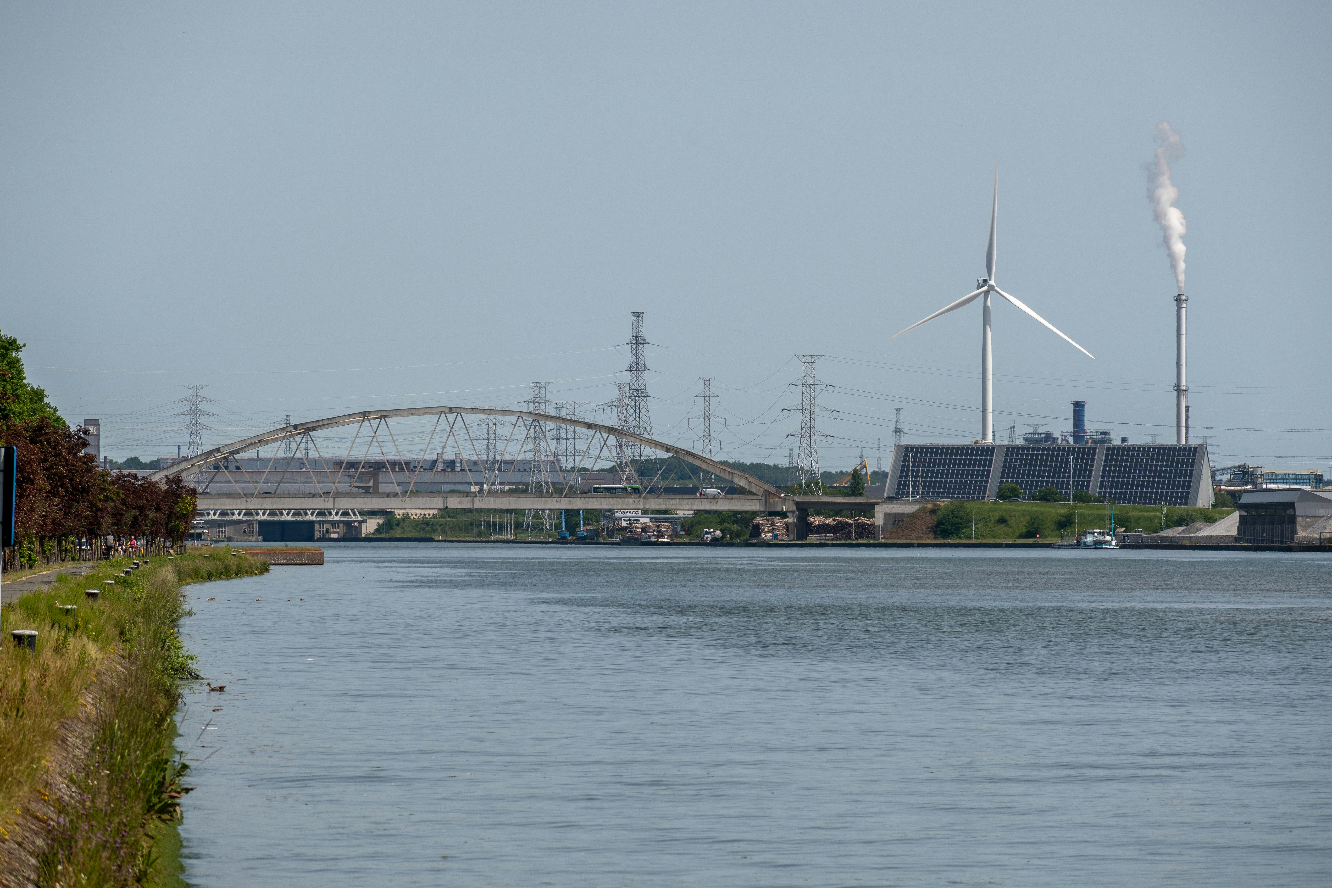 Industrial landscape with a bridge, wind turbine, and smoking chimneys.